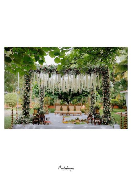The elegant wedding mandap, beautifully decorated with white floral drapes and set in a lush garden, ready for the sacred ceremony.