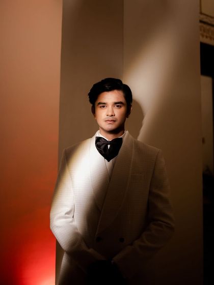 A striking portrait of the groom in a white tuxedo, illuminated by a single beam of light, creating a dramatic, high-contrast image.