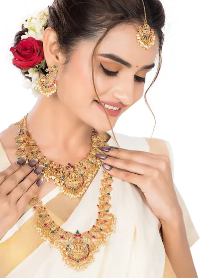 A model elegantly displays a layered South Indian temple jewellery set. The white saree with a gold border provides a classic backdrop, making the intricate gold work of the necklace and earrings stand out for catalogue photography.