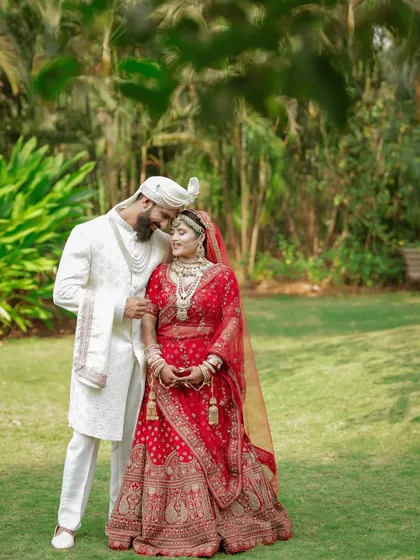 The groom's loving gaze and the bride's happy smile. This is a classic wedding portrait that beautifully captures the couple's connection amidst a lush green background.