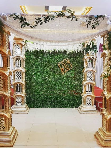 This mantap, designed for a baby shower, uses ornate pillars and a green foliage backdrop. A custom monogram with the couple's initials adds a personal touch to the traditional structure.