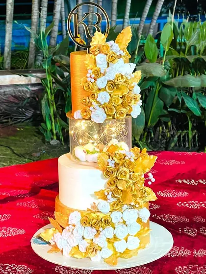 A magnificent white and gold wedding cake with a light-up separator tier. The golden sugar flowers cascade down the sides, creating a look of pure opulence and luxury.