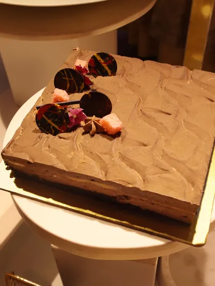 A square chocolate mousse cake with a textured finish and delicate chocolate garnishes.