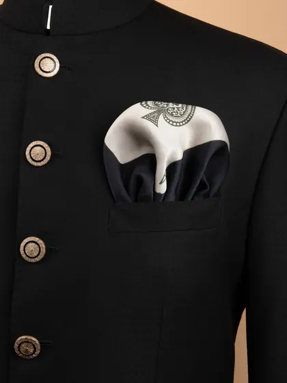 A close-up lifestyle shot showing a designer pocket square perfectly folded in the pocket of a sharp, black bandhgala jacket, demonstrating how to style the accessory.