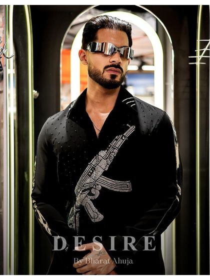 A confident pose in the gun-embroidered shirt, paired with futuristic eyewear for a look that is both edgy and high-fashion.
