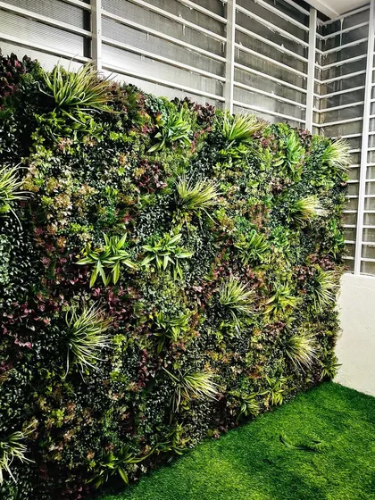 A lush green wall installed in a covered area next to a window. The artificial turf on the floor completes the look, creating a perfect all-weather garden spot.