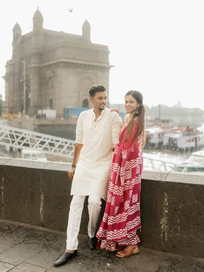 A classic pre-wedding portrait of the couple standing together with the Gateway of India in the background, showcasing their traditional outfits and the iconic Mumbai location.