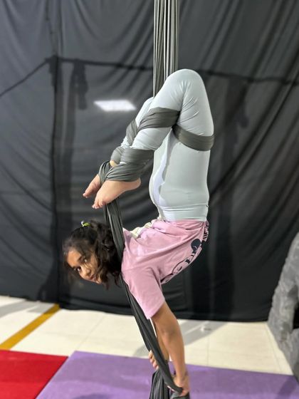 This young aerialist shows incredible flexibility, holding a challenging inverted pose with her feet wrapped securely in the silks.