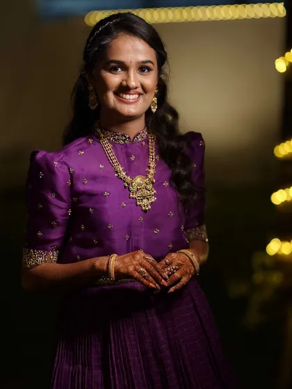 A happy client in a custom purple gown with puff sleeves and intricate gold embroidery.