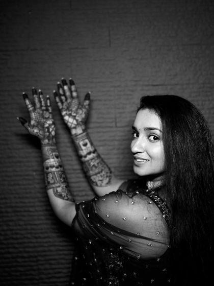 A playful black and white shot of the bride looking over her shoulder, her hands raised to display her beautiful mehendi.