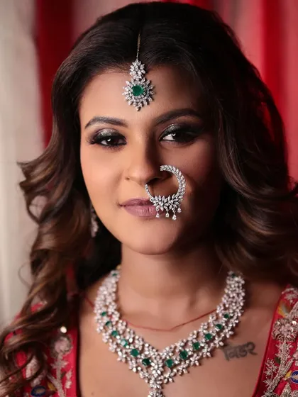 A full-face portrait of the bride, showcasing her flawless makeup, bold eyes, and stunning diamond and emerald jewellery set.