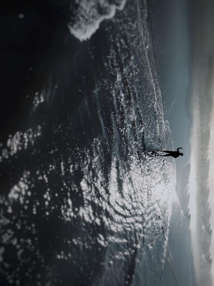 An artistic top down drone shot of a person standing on the shoreline in Goa. The contrast between the dark, wet sand, the white foam of the waves, and the lone figure creates a powerful and contemplative image.