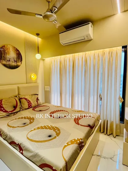 A modern bedroom with a beige upholstered bed and a stylish pendant light. The false ceiling with profile lighting and the simple, elegant curtains complete the look.