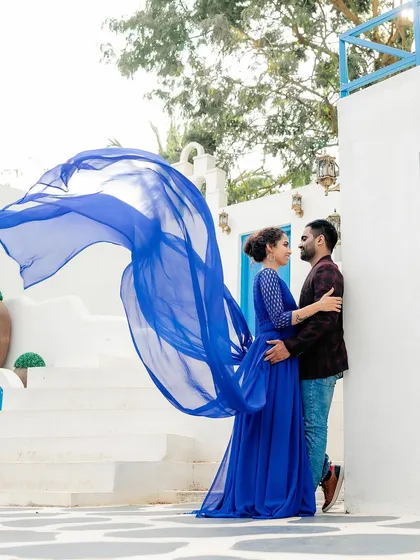 A stylish pre-wedding photo at a location with Greek-inspired architecture. The contrast of the bride's blue dress against the white walls creates a stunning visual.