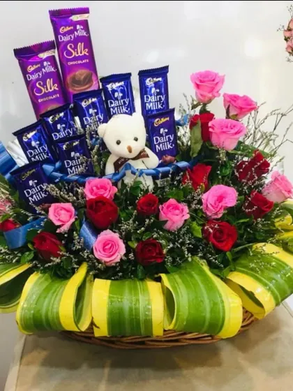 A slightly different angle of the chocolate and flower gift basket. This view shows how the teddy bear is nestled among the pink and red roses and Dairy Milk bars.
