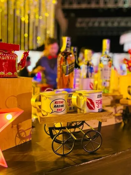 A close-up of the quirky details from my Bollywood bar. A hand-painted kettle and mugs with dialogues like "Kitne aadmi the?" sit on a decorative cart, creating perfect photo opportunities for your guests.