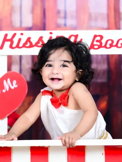 A happy baby girl in a "Kissing Booth" setup, perfect for a Valentine's or first birthday theme.