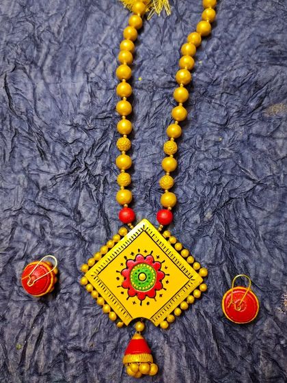A beautiful long necklace set in yellow and red, with a square pendant and a hanging jhumka. It's a bright and festive piece.