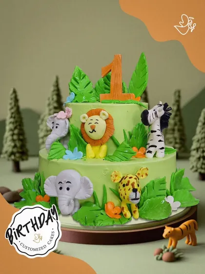 A wild first birthday cake. This two-tier jungle theme features a lion, zebra, elephant, and leopard, perfect for celebrating a little one turning one.