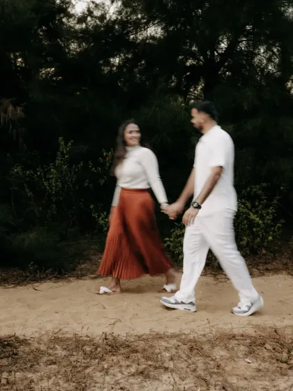 A couple enjoys a walk on a sandy path, their casual outfits and hand-in-hand stroll creating a relaxed and romantic vibe.