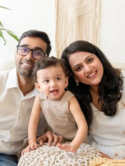 A classic family portrait with parents and their toddler smiling for the camera in a relaxed, indoor setting.