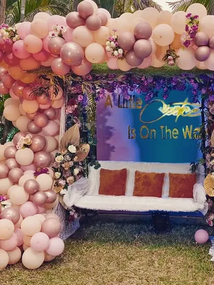 An outdoor baby shower with a whimsical "A New Chapter is on the Way" theme. This setup includes a decorated swing for the mom-to-be, a large balloon arch in pastel shades, and cute "Boy or Girl" props.