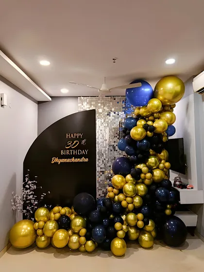 A sophisticated 30th birthday decoration for a home party. This setup uses a bold black and gold color scheme with a custom backdrop, a silver sequin panel, and an elaborate balloon cascade.