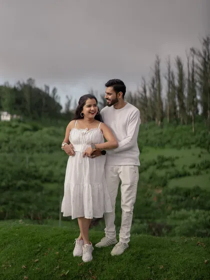 A beautiful portrait of the couple in the Ooty hills, sharing a happy and relaxed moment. The coordinating white outfits stand out beautifully against the green backdrop.