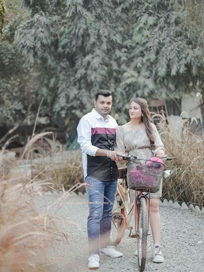A standing pose with the bicycle prop, capturing a quiet, romantic look between the couple amidst the wild grass. This highlights a different mood for an outdoor couple photoshoot.