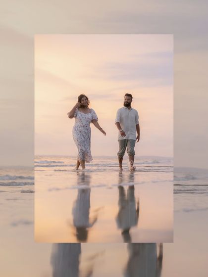 A beautiful, soft-lit portrait of the couple walking by the water's edge. The reflection in the wet sand and the pastel colors of the sunset create a dreamy, romantic image.