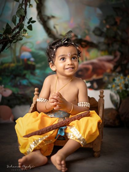 A playful little Krishna in a magical forest setting. His expression is full of mischief and fun.