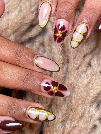 A detailed shot of the brown and gold abstract floral nail art. The combination of the dark base and metallic gold is incredibly chic.