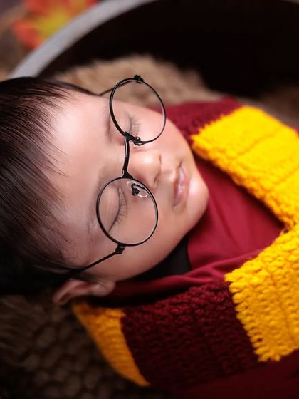 A close-up on our newborn Harry Potter, focusing on his peaceful face, iconic glasses, and cozy Gryffindor scarf.