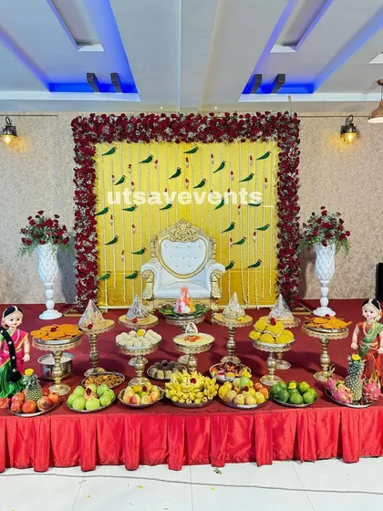 Here is a vibrant and classic baby shower decoration. The stage is set with a bright yellow backdrop adorned with hanging parrot motifs and framed by a rich border of red roses, creating a festive and traditional South Indian look.