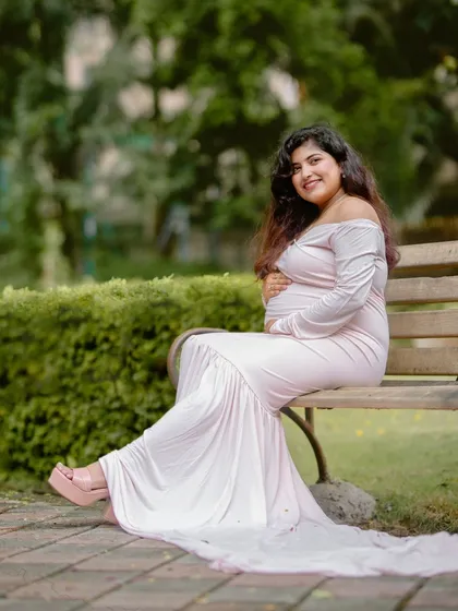 A graceful portrait of an expecting mother seated on a park bench, her flowing dress creating a beautiful silhouette.