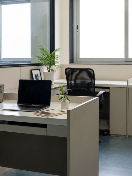 Workstations are designed with minimalism and functionality in mind, featuring clean white desks, ample natural light from large windows, and an uncluttered layout to enhance employee well-being.