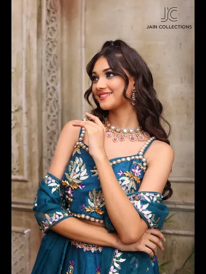 Another smiling shot of a model in the teal floral lehenga, showcasing its off-shoulder blouse design and vibrant colors.