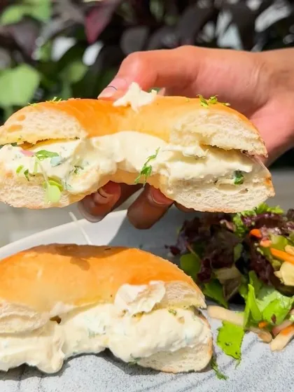 A closer look at our Garlic Cream Cheese Bagel, sliced in half to show the generous, creamy filling. It's served with a fresh side salad.