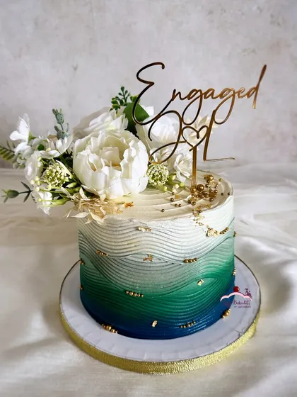 A pretty floral engagement cake with an ombre effect in shades of green, blue, and grey. The textured buttercream and gold flakes add a modern, artistic touch.
