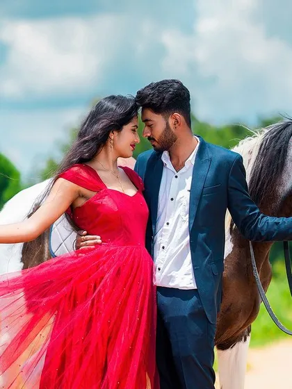 A fairytale pre-wedding moment captured in a vibrant, cinematic style. The flowing red dress against the lush green landscape and the presence of a beautiful horse adds a touch of epic romance.