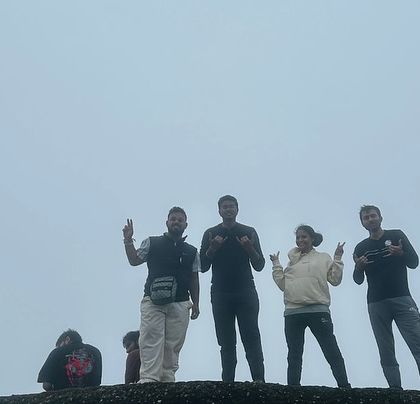 Trekkers posing on a rock at the Skandagiri summit, with a thick blanket of fog creating a dramatic backdrop.