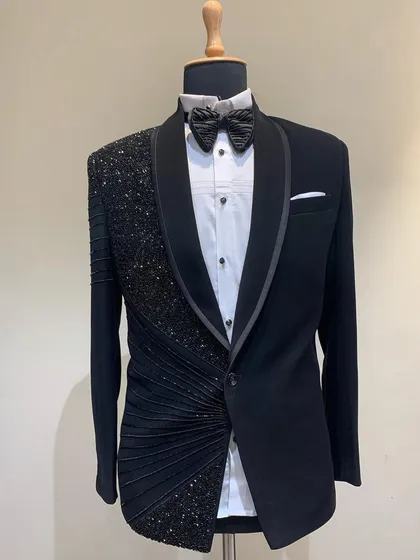 A jet black tuxedo designed for an engagement or ring ceremony. It features a draped, pleated design on one side, embellished with black sequins for a dramatic effect.