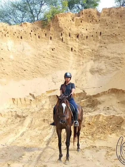 A rider stands confidently on her horse against the backdrop of a sandy cliff. This showcases the adventurous spirit of our trails and the incredible trust between our riders and horses.