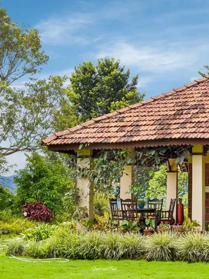 The exterior of Villa Magnolia in Virajpet, a traditional home with a tiled roof and a sprawling veranda. The lush garden and manicured lawn create a serene and picturesque setting.