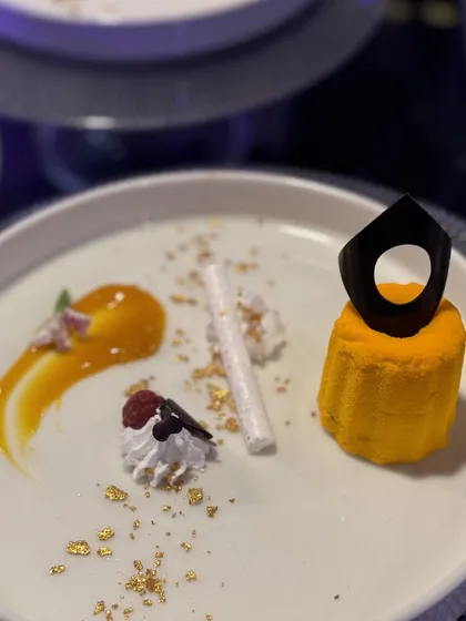 A mango mousse dessert, elegantly shaped and placed on the plate with a smear of sauce and delicate garnishes. A true taste of edible luxury.