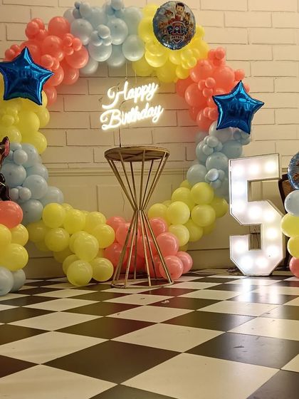 This Paw Patrol themed decoration is ready for action. It features a circular balloon arch in the show's primary colors, character balloons of Chase and others, a neon birthday sign, and a light-up number '5'.