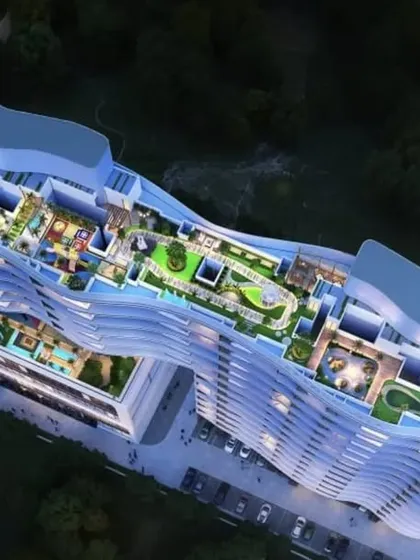 An aerial view of the podium level of our Tropicano project in Guwahati. The rooftop is designed as a complete recreational zone with pools, gardens, and play areas, all following the signature curved facade of the building.