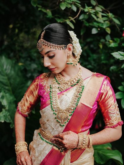 A bride adjusts her traditional jewelry, with the lush green foliage of our garden behind her. This shot highlights the beauty of both the bride and the natural surroundings.