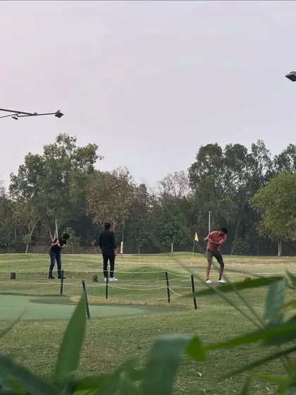 A view of the putting green from a distance, showing players working on their short game.