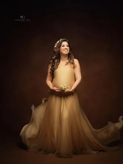 A hopeful and dreamy portrait in a golden gown. The mother-to-be looks up, holding a small bouquet, creating a sense of gentle anticipation.